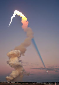 Airplane Picture - Shuttle launch of Atlantis at sunset in 2001. The sun is behind the camera, and the plume's shadow intersects the moon across the sky.