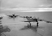 Airplane Picture - A Fairey Firefly takes off from HMS Illustrious in the River Clyde in 1943. In the background a Sabre-engined Firebrand Mk.II is running up its engine on the deck lift.