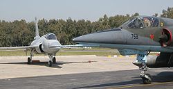 Airplane Picture - A Mirage 5 ROSE fighter taxiing during flight operations at a Pakistan Air Force airbase. The FLIR sensor housing under the cockpit can be clearly seen. Parked in the background is a JF-17 fighter.